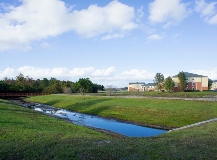 Retention Pond with grass area and red bridge, trees and building exteriors in the background